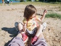 Small girl with red sneakers sitting at her mother& x27;s legs at beach. Royalty Free Stock Photo