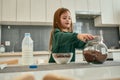 A small girl screwing a cap of a cereal balls glassy pot standing in a large kitchen