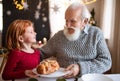 Small girl with senior grandfather indoors at home at Christmas, talking.