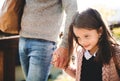 A small girl with unrecognizable father walking outdoors in park in autumn.