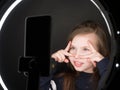 Small girl using camera of smartphone in front of ring light, shooting video for blog. Adorable child learning new technology.