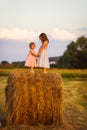 Small girls stand on a hay stack on wheat field