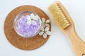 Small glass bowl with purple bath salt (foot soak), massage body brush and white flowers. Top view, copy space Royalty Free Stock Photo