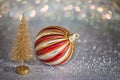 Small gold Christmas tree and striped christmas ball on a silver surface with defocused background with bokeh lights. Royalty Free Stock Photo