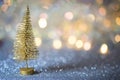 A small gold Christmas tree on a silver surface with defocused background with bokeh lights. Royalty Free Stock Photo