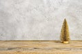 Small golden Christmas tree on a wooden surface, in front of a white wall, with space for text Royalty Free Stock Photo