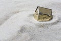 Small golden model house sinking into the sand, concept of risk Royalty Free Stock Photo