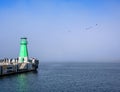 Green lighthouse, fog and blue water in contrasting sunlight