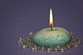 Small Green Lit Candle Surrounded by Beads Against Purple Background Royalty Free Stock Photo