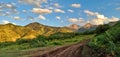 A small green meadow, located at the foot of the mountains, the peaks of which are illuminated by the rays of the sun at sunset.