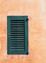 Small green painted closed wooden shutter on an ochre orange old rough textured wall in bright sunlight and shadow Royalty Free Stock Photo