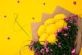 Small green sprig in the shape of a number eight and a large bouquet of lush chrysanthemum flowers on bright yellow background.