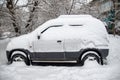 A small grey car covered with snow in a winter CIS city