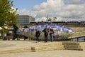 A small group of tourists chat together and compare notes beside the Salmon of Knowledge fish sculpture Belfast.