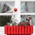 Window sill with Christmas decoration in red flower box. Small Christmas tree, red ball and red and white candy cane.