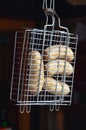 A small hand grill is filled with fried thick sausages on a dark background