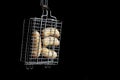 A small hand grill is filled with fried thick sausages on a dark background