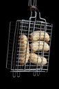 A small hand grill is filled with fried thick sausages on a dark background