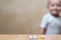 A small handful of pills on the table and a blurred baby in the background, copy space