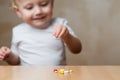 A small handful of pills on the table and a blurred baby in the background