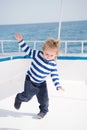 Small happy baby boy dancing on yacht in marine shirt