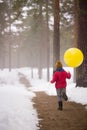 A small happy boy in jeans and a red sweater running in the winter forest and holding a big yellow balloon. Birthday boy Royalty Free Stock Photo