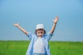 Small happy boy (5 years old) raises his hands ad smile against blue sky and green grass. High quality photo Royalty Free Stock Photo