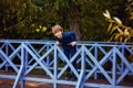 A small happy Caucasian child in a sweater and trousers poses against a wooden bridge in the open air in a Park