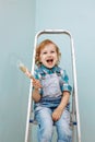 A small happy child sits on a stepladder and holds a brush with paint. Royalty Free Stock Photo