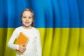 Small happy curious child girl holding book against flag of Ukraine background. Learn Ukrainian language. School and education Royalty Free Stock Photo