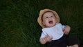 Small Happy Newborn child in summer panama hat Fall down laying on grass barefoot in Summer Sunny Day. Infant Kid Royalty Free Stock Photo