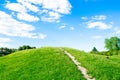 Small hiking trail, path climbing up the mountain, hill, mound with green grass against bright blue sky with clouds Royalty Free Stock Photo