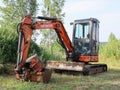 Small Hitachi Excavator on empty green area for construction in countryside in summer, front view