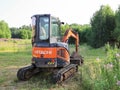 Small Hitachi Excavator on empty green area for construction in countryside in summer, rear view