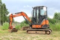Small Hitachi Excavator on empty green area for construction in countryside in summer, side view