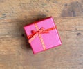 Small holiday gift in square red color box, covered with ribbon with bow on wooden background top view Royalty Free Stock Photo