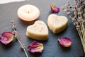 Small homemade heart shape bath melts in bathroom on black stone tray with candle burning and dried rose petals. Royalty Free Stock Photo