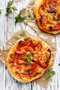 Small homemade vegetable pizza with addition of grilled pepper, tomatoes, cheese and herbs on a white wooden table