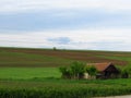 A small house surrounded by green field grass and tilled field. Ploughed cultivated ground. Countryside.