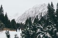 Small human figures walking towards High Tatra mountains through pine tree forest in winter, Slovakia Royalty Free Stock Photo