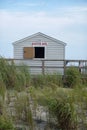 Small hut on a sandy beach surrounded by tall grass with it`s window opened with a sign that says,