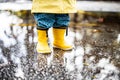 Small infant boy wearing yellow rubber boots and yellow waterproof raincoat standing in puddle on a overcast rainy day Royalty Free Stock Photo
