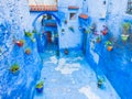 Small inner yard in Chefchaouen, Morocco with colorful flowerpots on blue walls