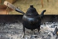 Small iron water kettle on three legs with a wooden handle for boiling coffee or tea on open fire or charcoal embers, copy space,