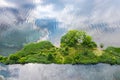 Small island in middle of lake with green trees and rippled water with sky reflections. aerial top view