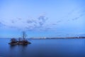 Small island in smooth lake at dusk hiding a nesting swan, safely removed from vibrant cityscape in the distance across the water Royalty Free Stock Photo