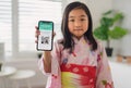 Small japanese child with traditional costume showing covid-19 vaccination certificate on smartphone.