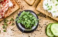 Small jar with basil microgreen sprouts and sandwiches with cream cheese, microgreens, cucumber and spices on cutting board.