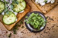 Small jar with basil microgreen sprouts and sandwiches with cream cheese, microgreens, cucumber and spices on cutting board.