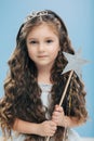 Small kid angel has long crisp hair, blue eyes, holds magic wand in form of star, poses over blue background, has appealing Royalty Free Stock Photo